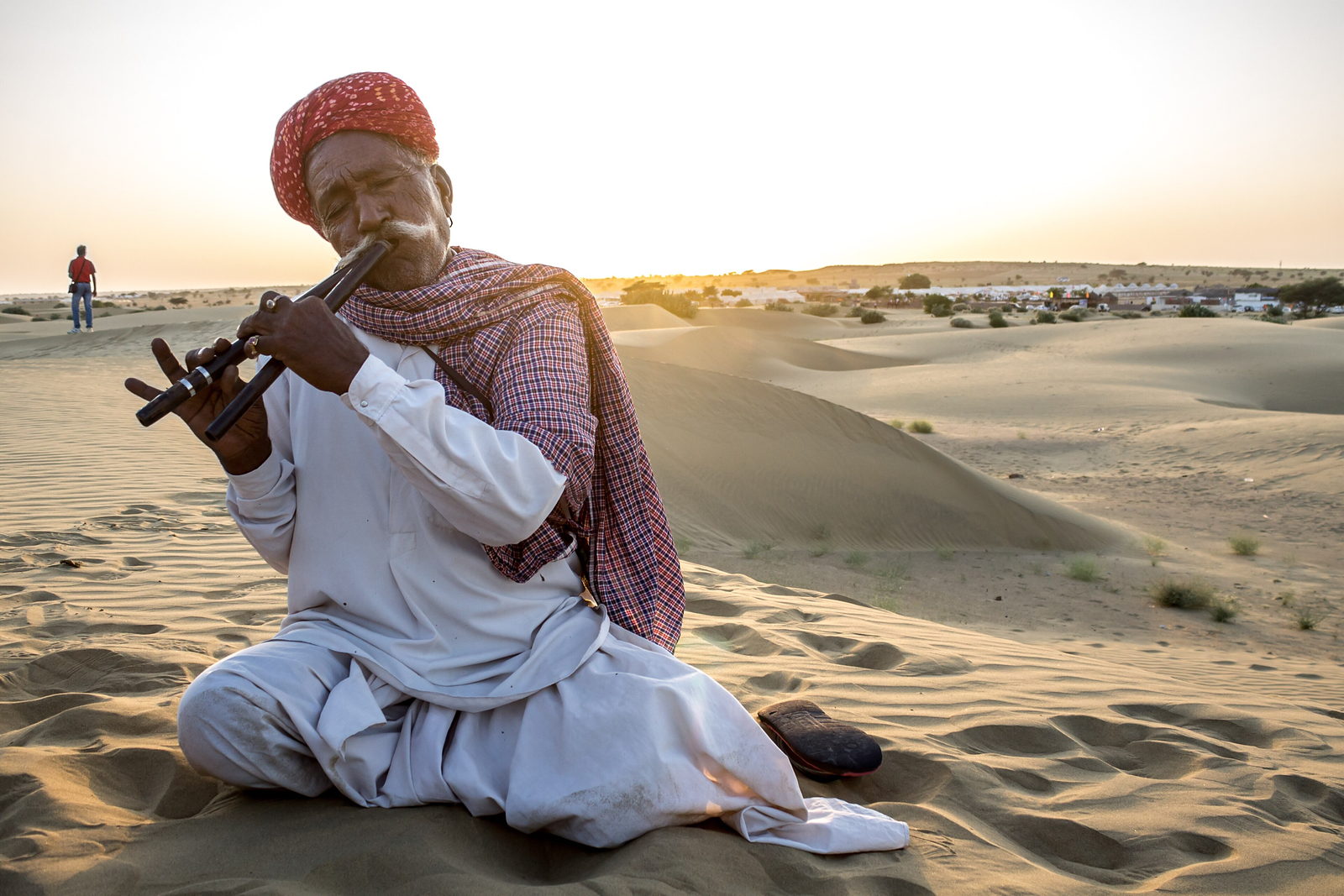 Folk musician playing the flute on the dunes as the sun sets